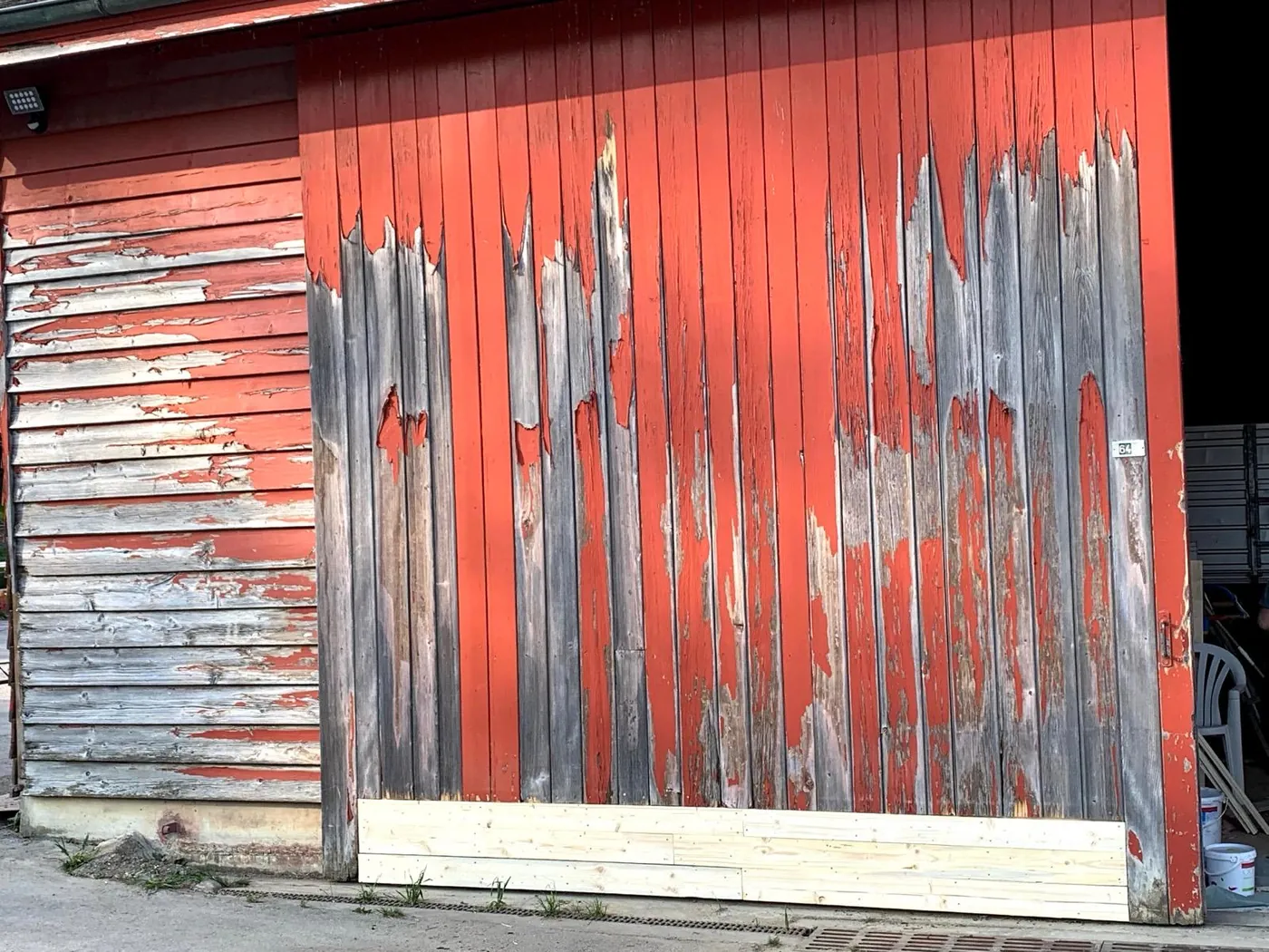 Porte de grange avant : bois gris, peinture rouge partie par plaques.