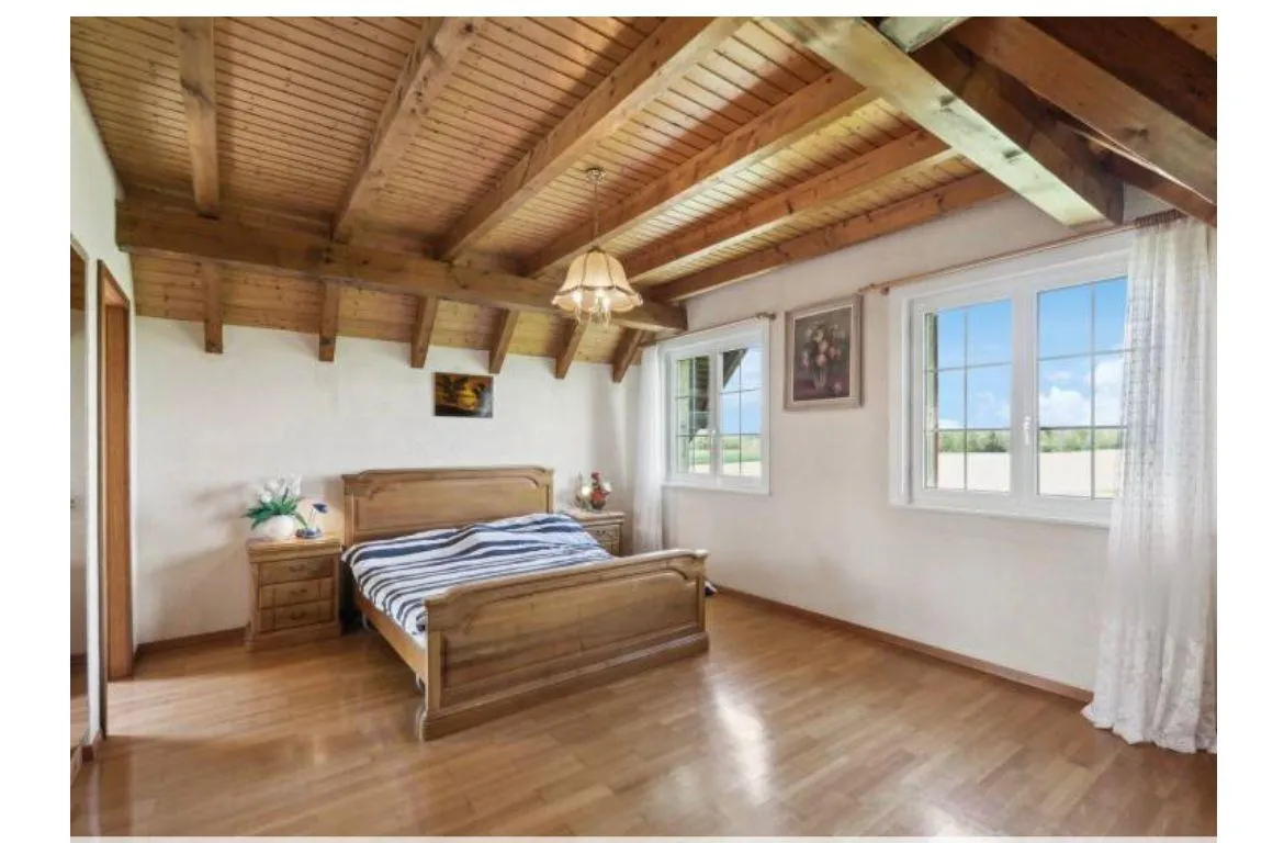 Chambre avec plafond à poutres apparentes et parquet.
