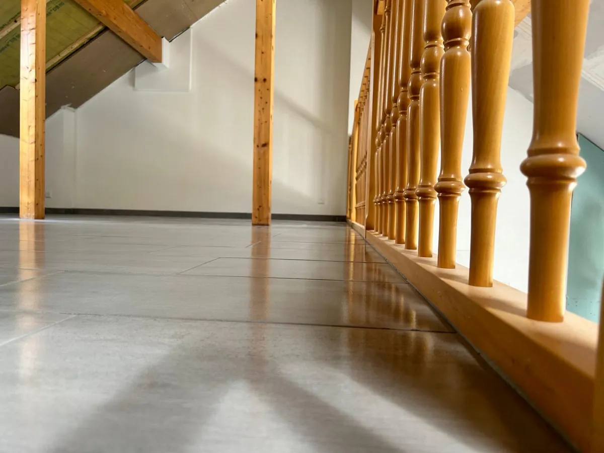 Couloir sous combles avec balustrade en bois et sol coulé.