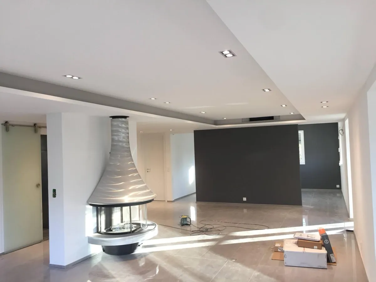Séjour avec cheminée centrale suspendue, murs clairs et plafond structuré.