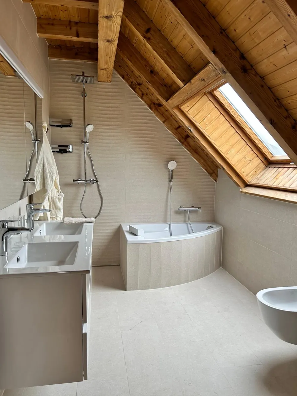 Salle de bains sous combles avec poutres apparentes et baignoire d'angle.