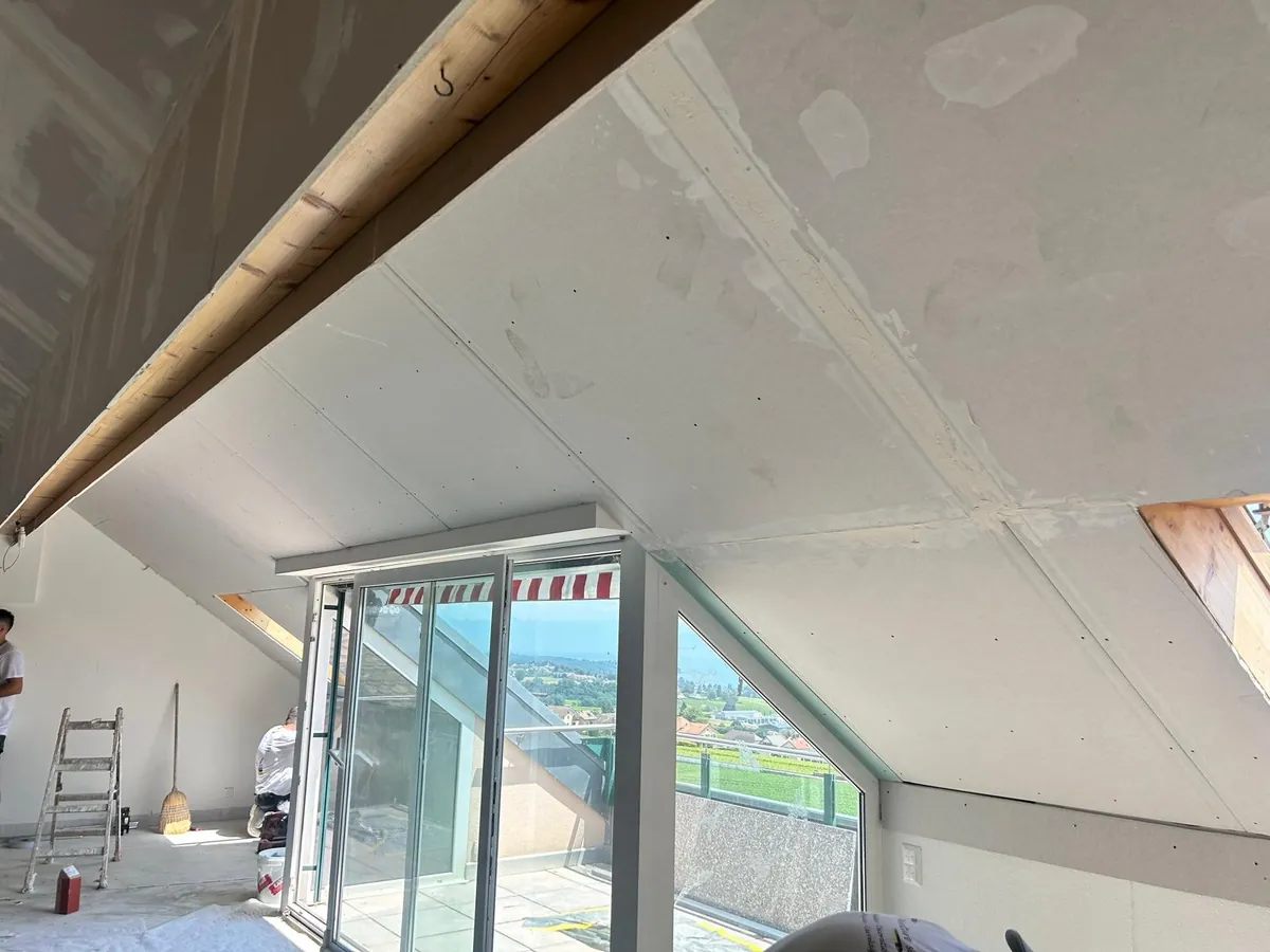 Pièce sous combles ouverte sur une grande baie vitrée, murs et plafond repris.